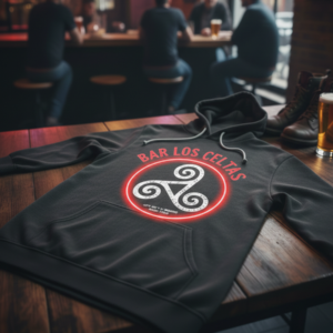 black hoodie featuring a "Bar Los Celtas" logo with a triskelion symbol sits on a wooden table in a dimly lit bar.